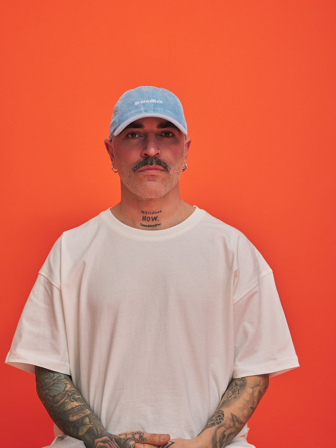 Man wearing a light blue cap and white t-shirt against an orange background