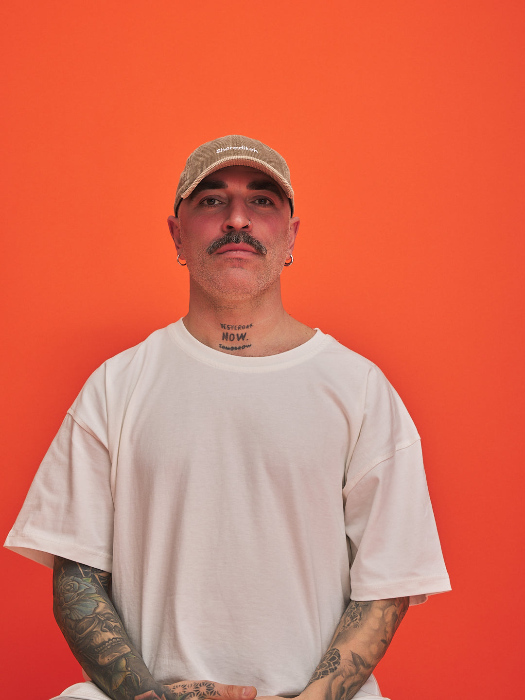 Man wearing a beige cap and white t-shirt against an orange background
