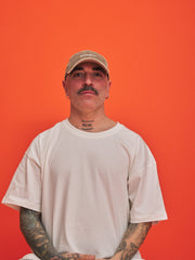 Man wearing a beige cap and white t-shirt against an orange background