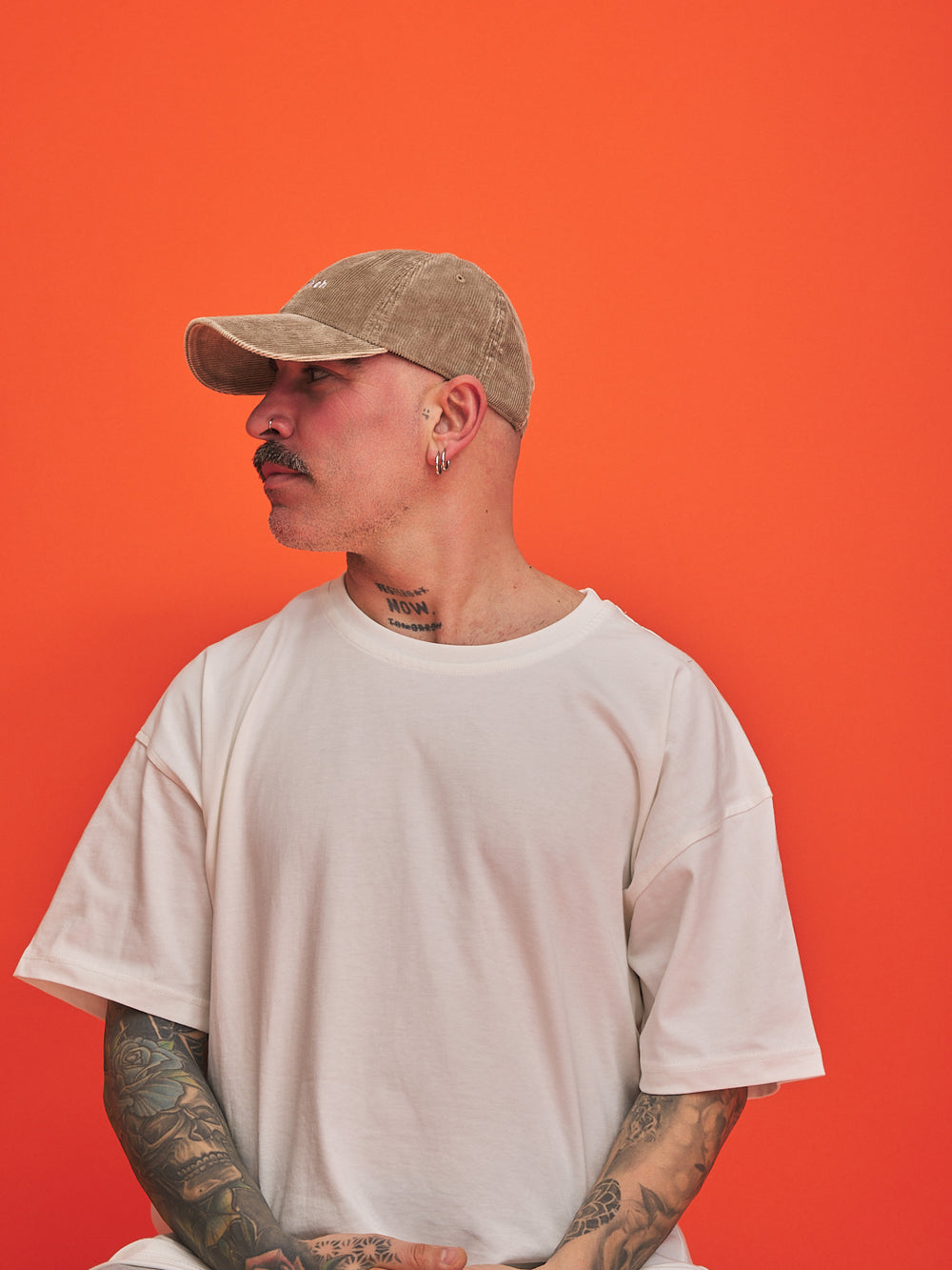 Person wearing a beige cap and white t-shirt against an orange background