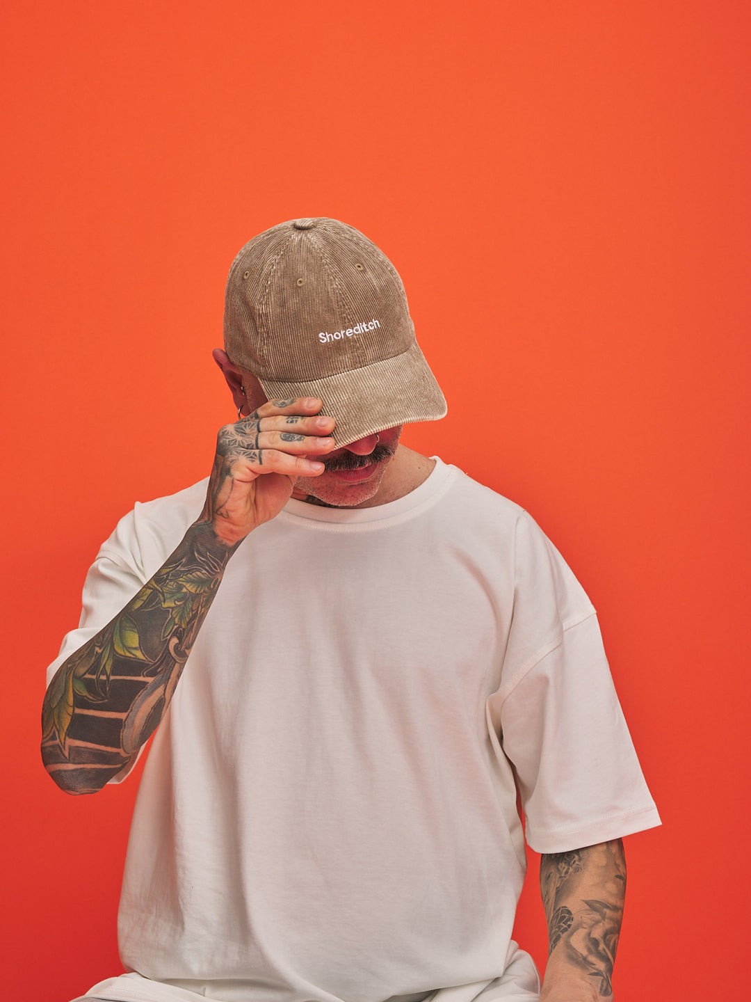 Person wearing a cap and white t-shirt against an orange background