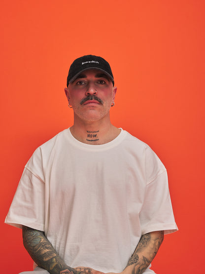 Man wearing a black cap and white t-shirt against an orange background