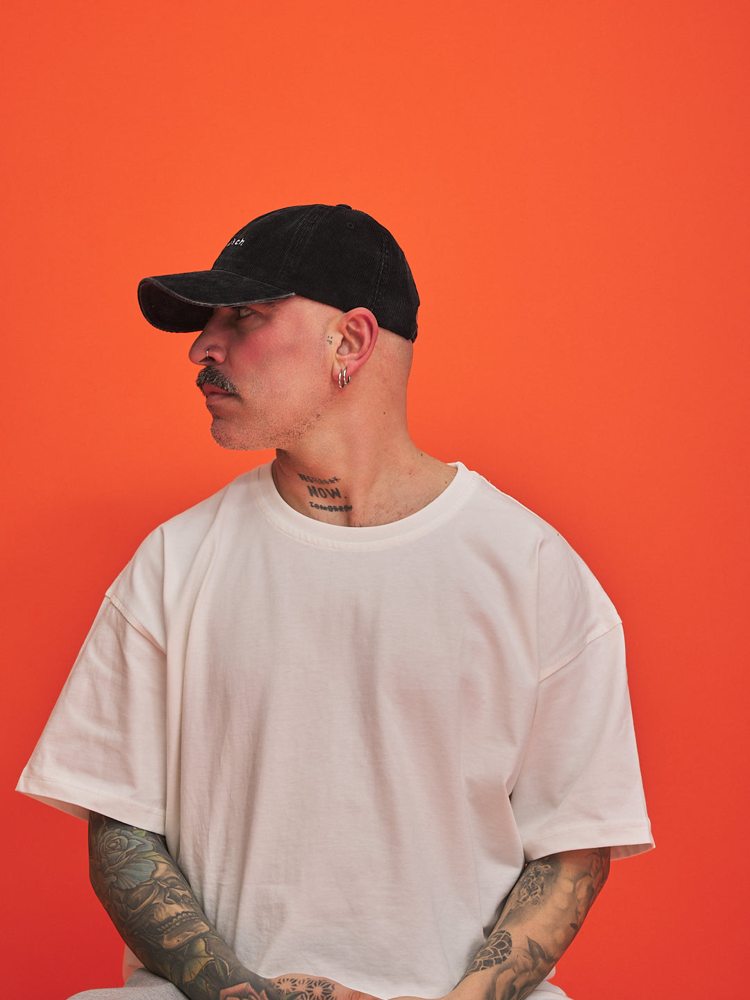 Man wearing a black cap and white t-shirt against an orange background