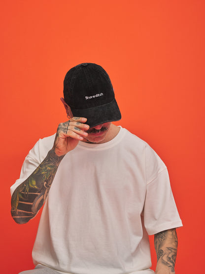 Person wearing a black cap with 'Shoreditch' logo on an orange background