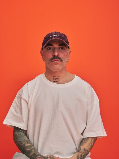 Man wearing a white t-shirt and burgundy cap against an orange background