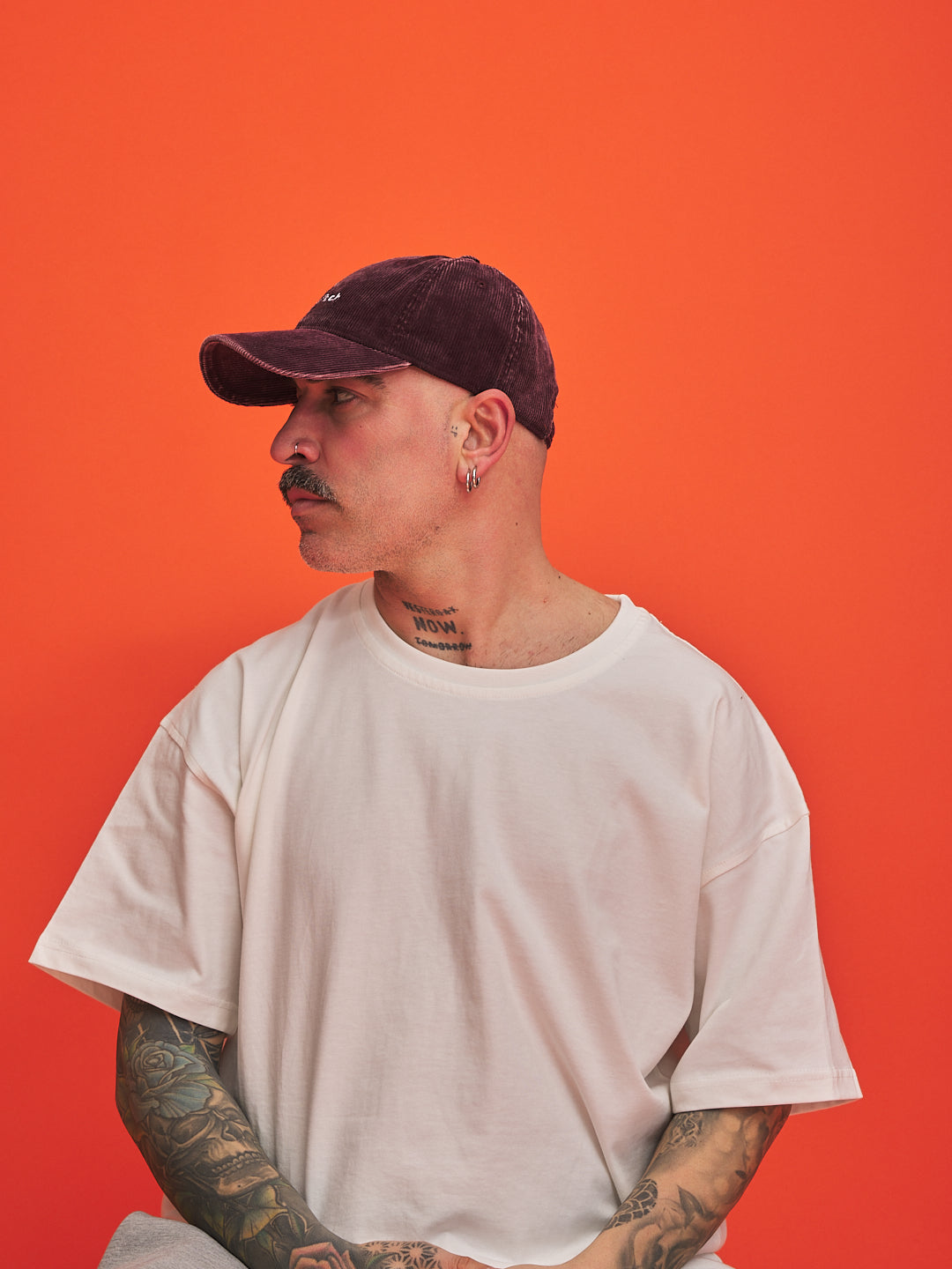 Man wearing a white t-shirt and burgundy cap against an orange background