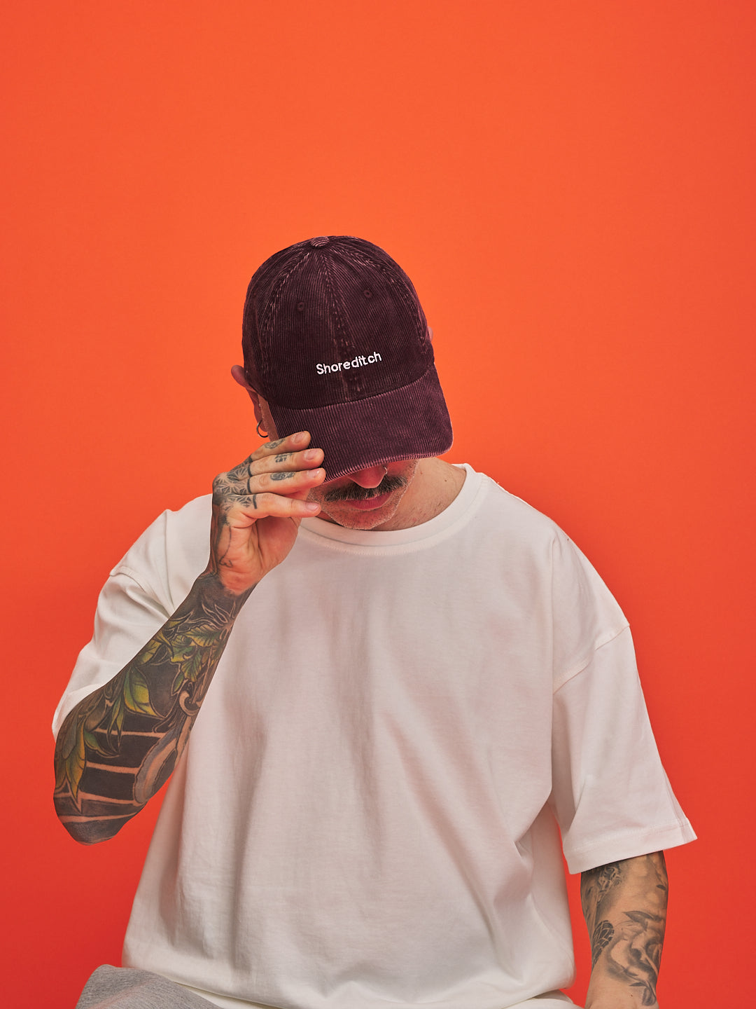 Person wearing a maroon cap with 'Shoreditch' logo against an orange background