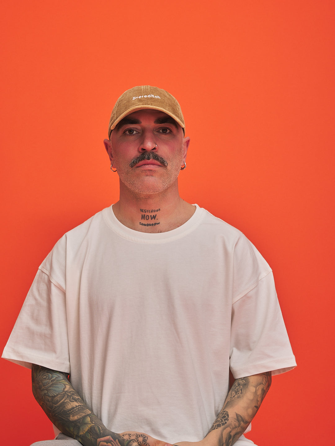 Man wearing a camel cap and white t-shirt against an orange background