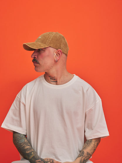 Man wearing a camel cap and white t-shirt against an orange background