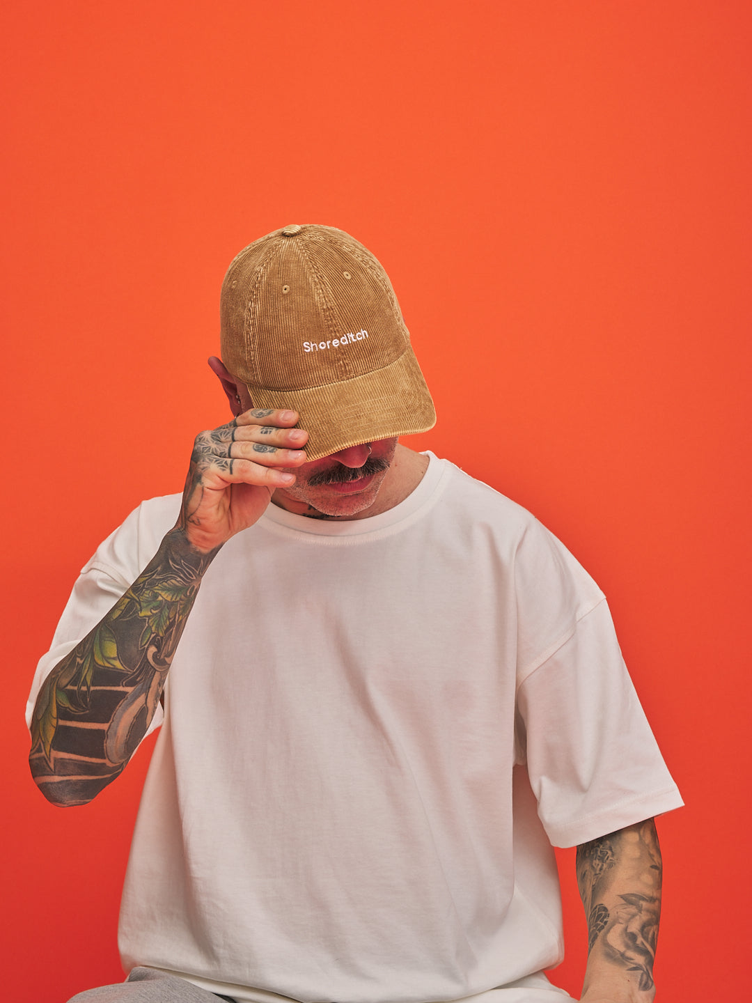 Person wearing a camel cap with a logo on an orange background