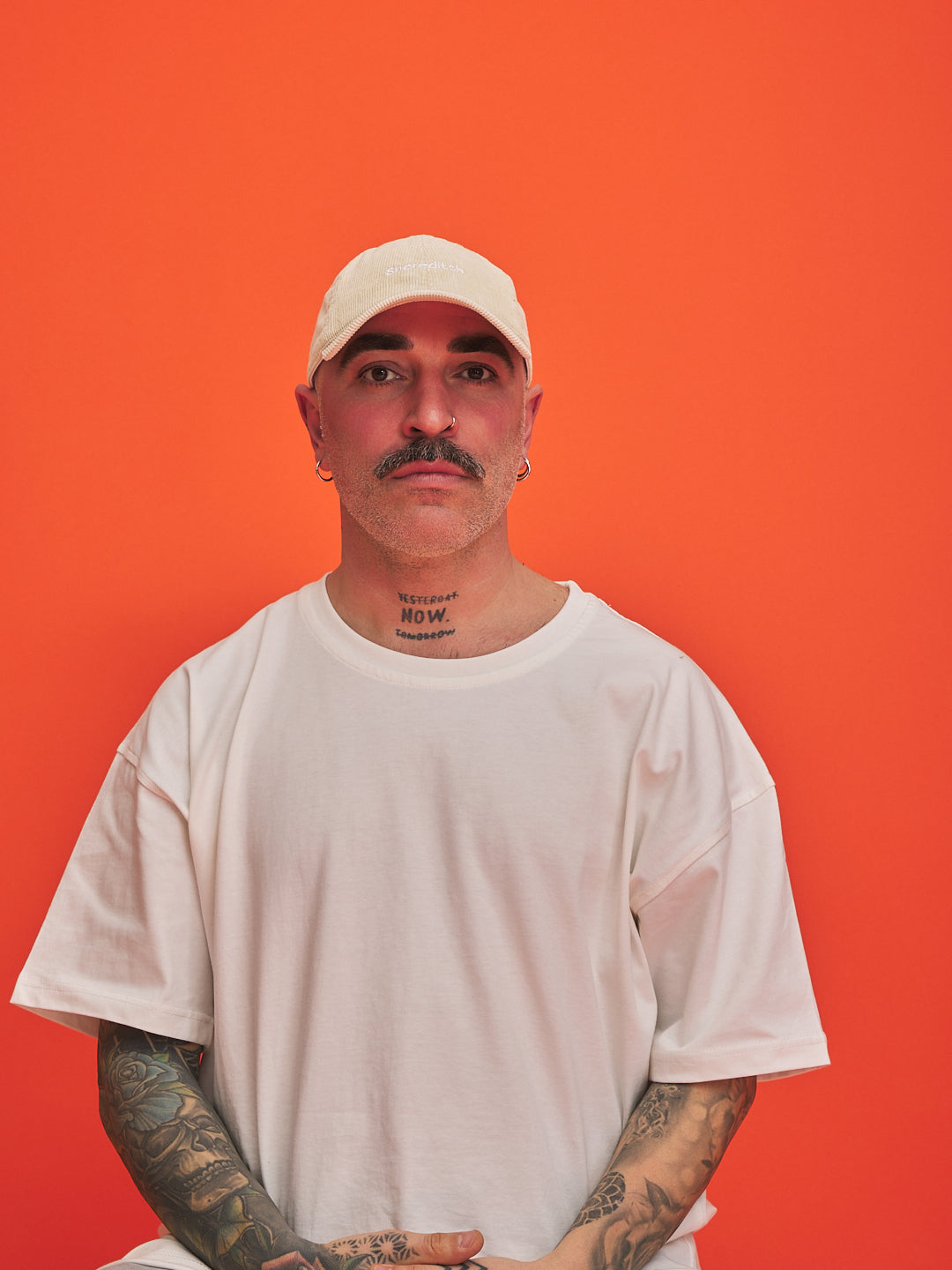 Man wearing a cream cap and t-shirt against an orange background