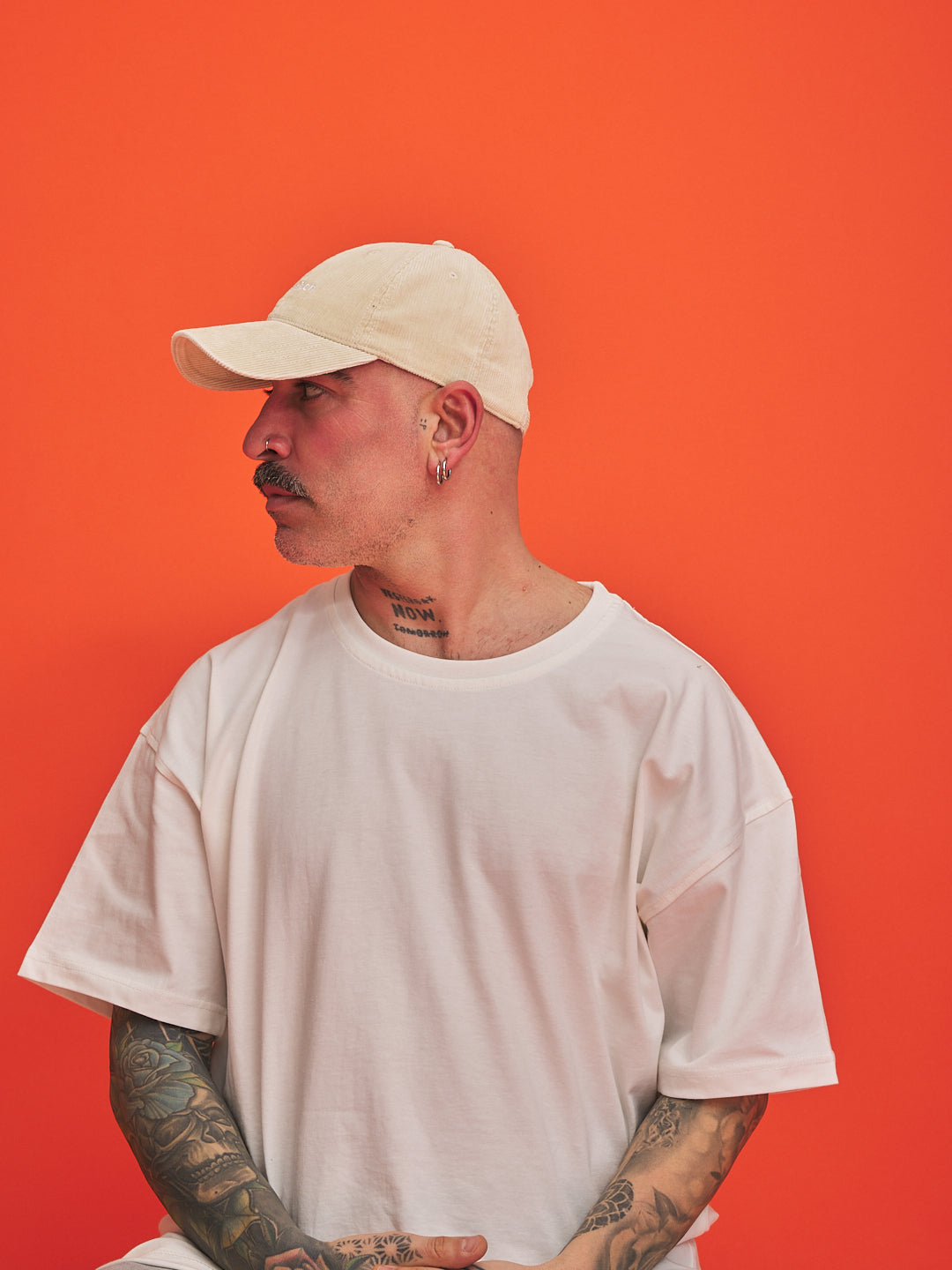 Man wearing a cream cap and white t-shirt against an orange background