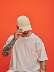 Person wearing a cream cap and white t-shirt against an orange background