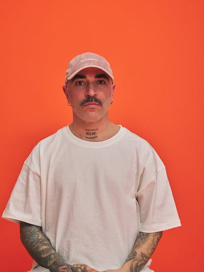 Man wearing a pink cap and white t-shirt against an orange background