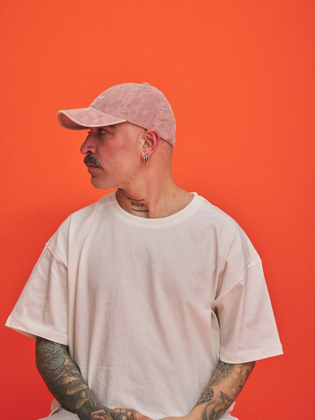 Person wearing a light pink cap and white t-shirt against an orange background