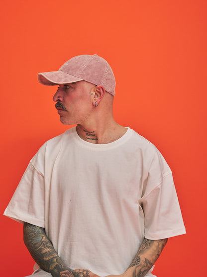 Person wearing a light pink cap and white t-shirt against an orange background