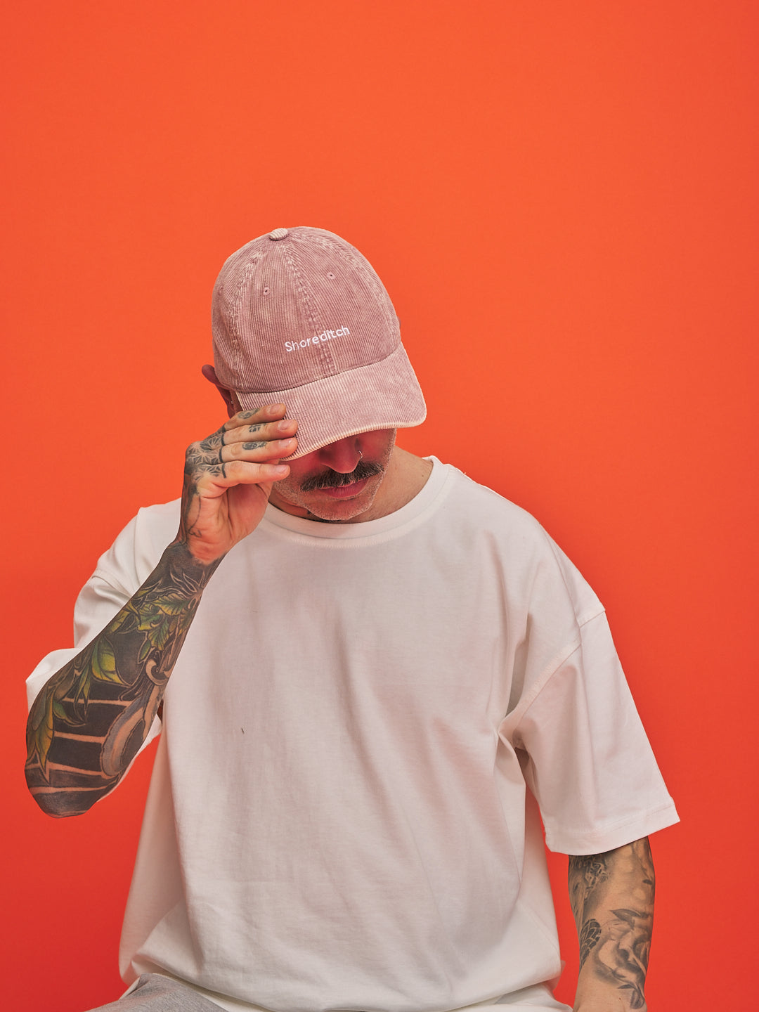 Person wearing a pink cap and white t-shirt against an orange background