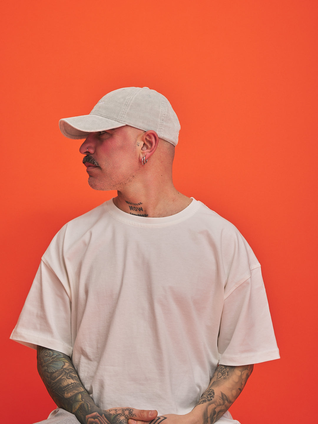 Person wearing a light grey cap and t-shirt against an orange background