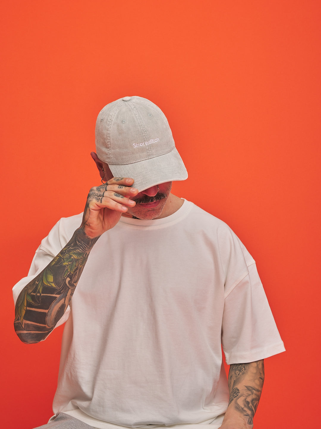 Person wearing a cap and white t-shirt against an orange background
