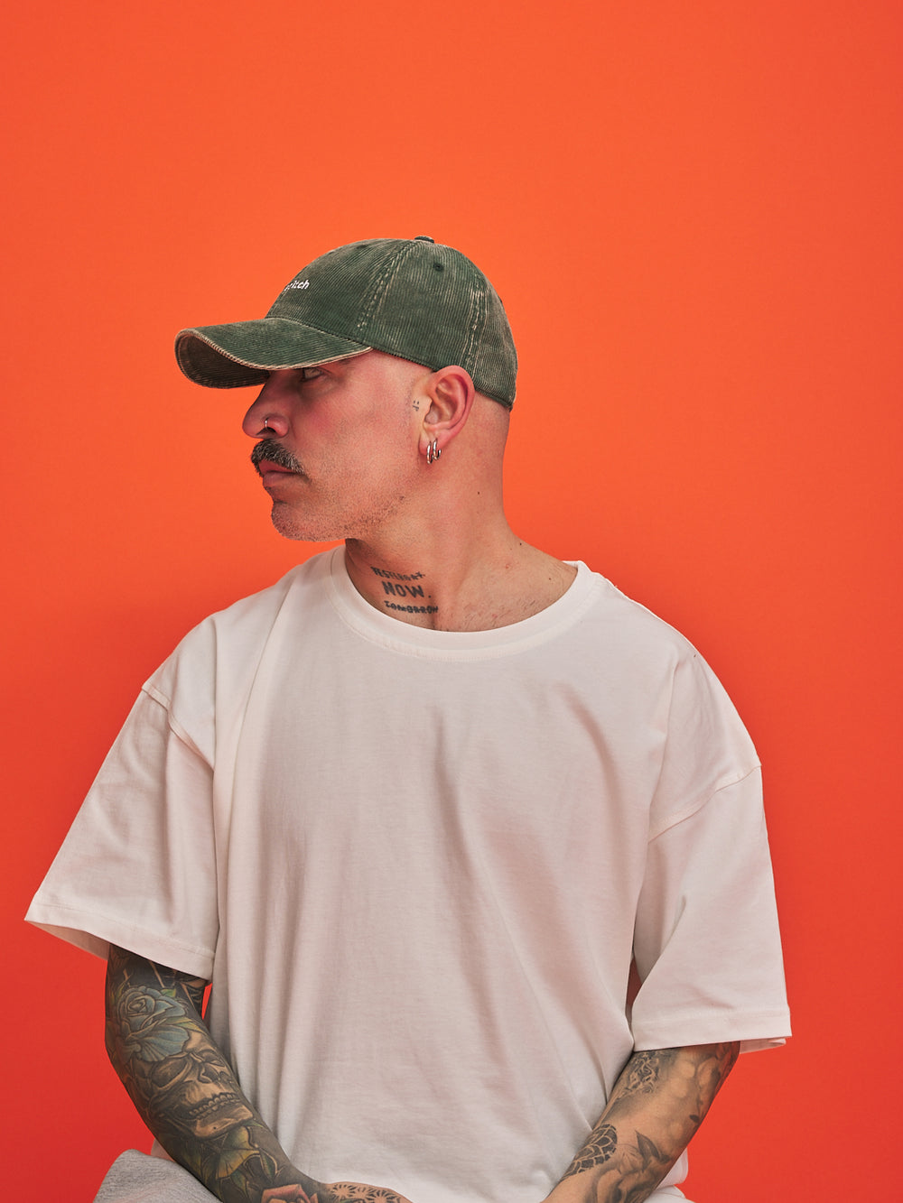 Man wearing a green cap and white t-shirt against an orange background