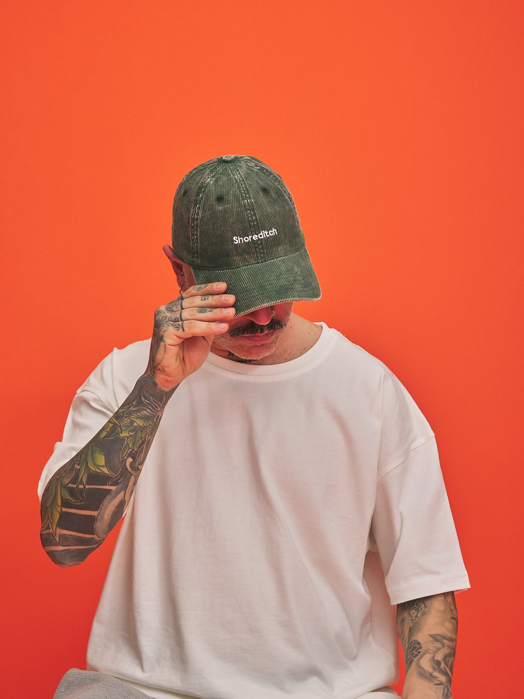 Person wearing a green cap with 'Shoreditch' text on an orange background