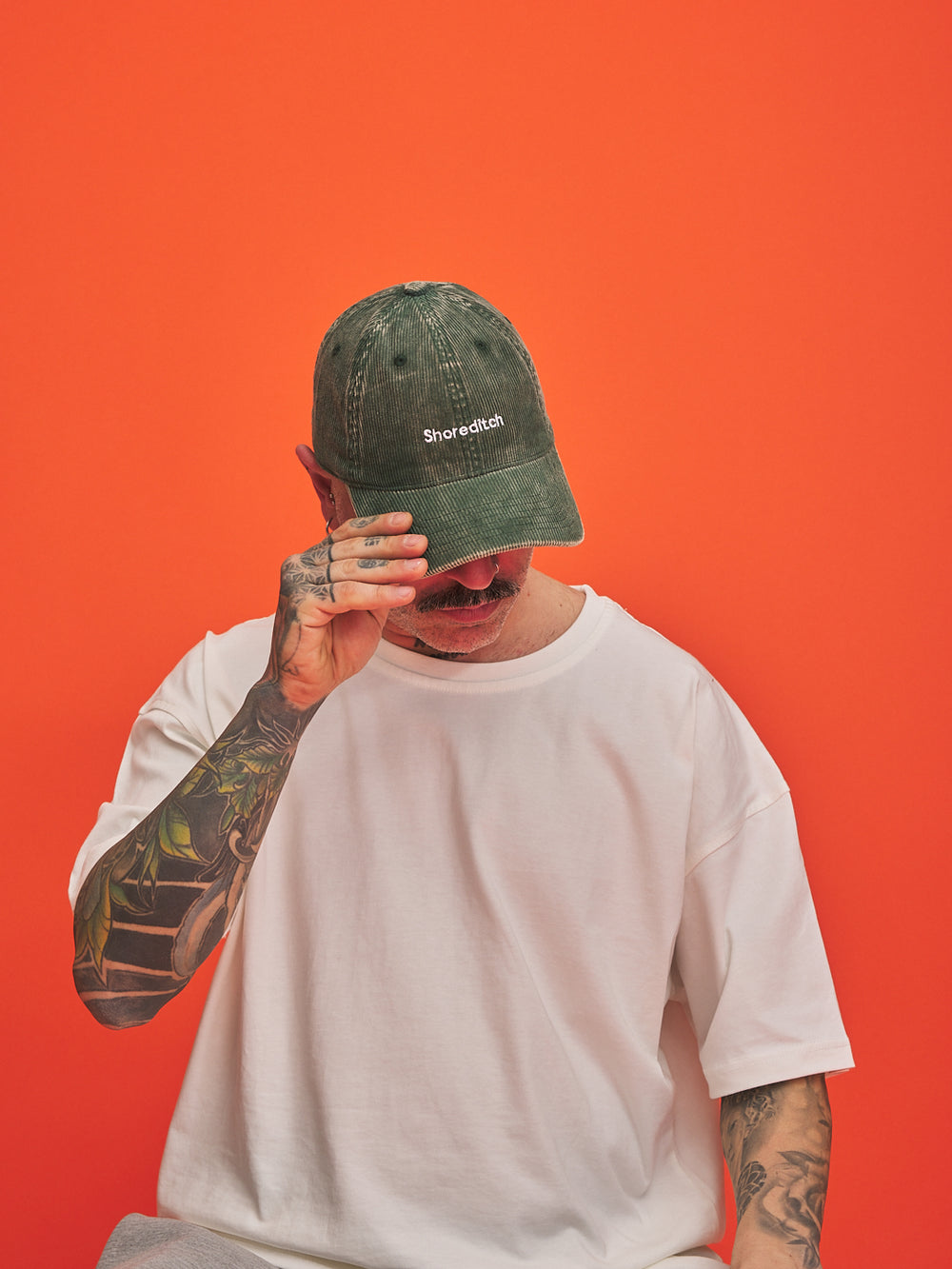 Person wearing a green cap with 'Shoreditch' text on an orange background