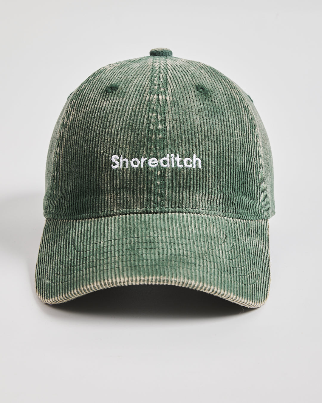 Green corduroy cap with 'Shoreditch' text on a light gray background