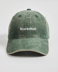 Green corduroy cap with 'Shoreditch' text on a light gray background