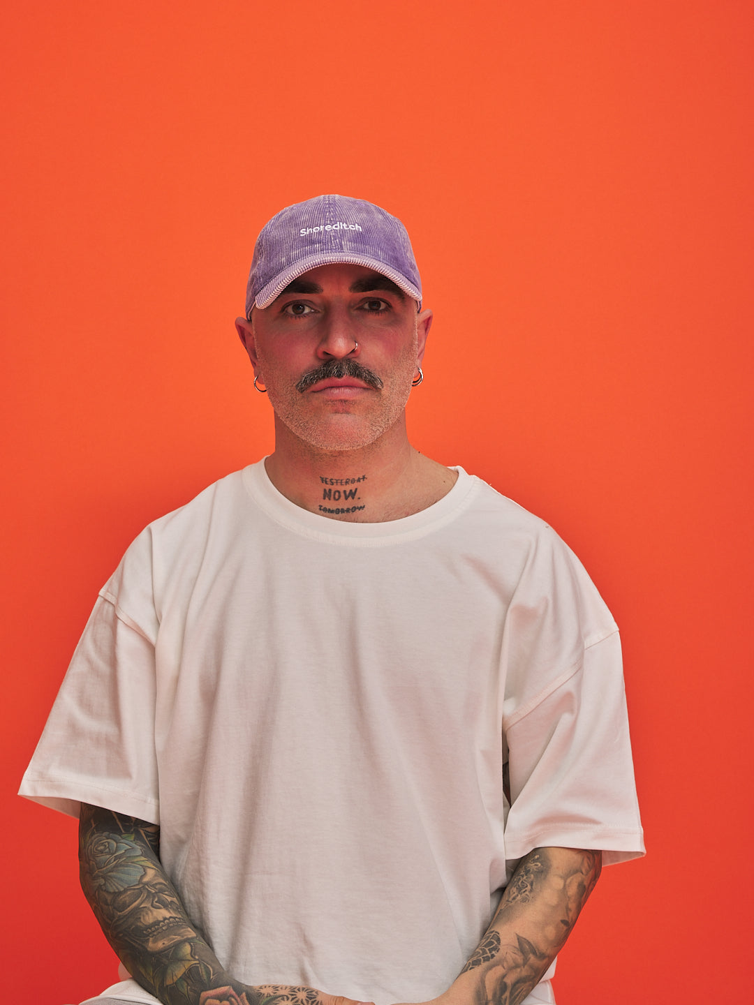 Person wearing a white t-shirt and purple cap against an orange background
