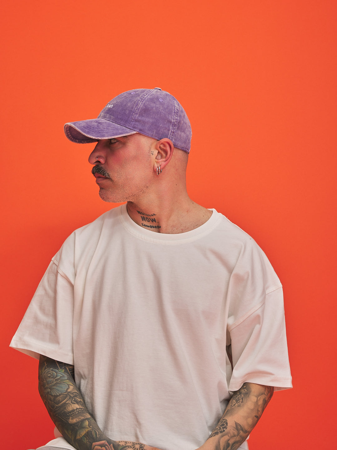 Person wearing a white t-shirt and purple cap against an orange background