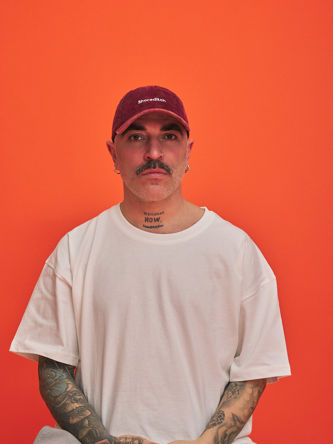 Man wearing a white t-shirt and red cap against an orange background