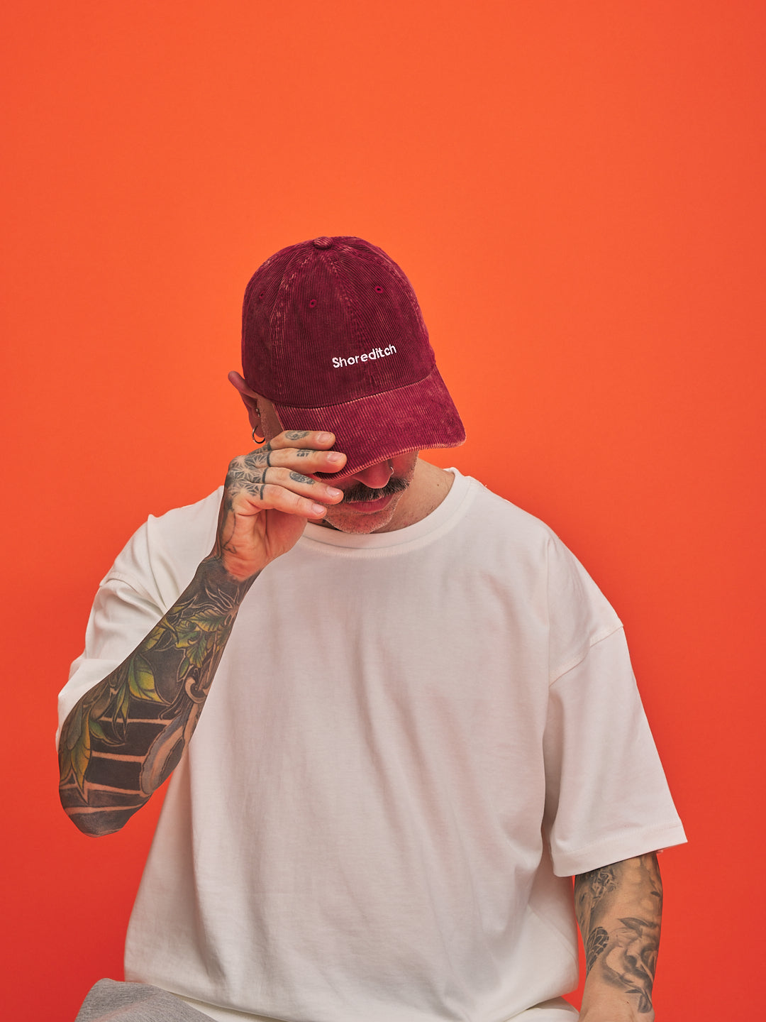 Person wearing a maroon cap with 'Shoreditch' logo against an orange background