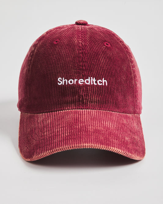 Red corduroy cap with 'Shoreditch' embroidered on a light gray background