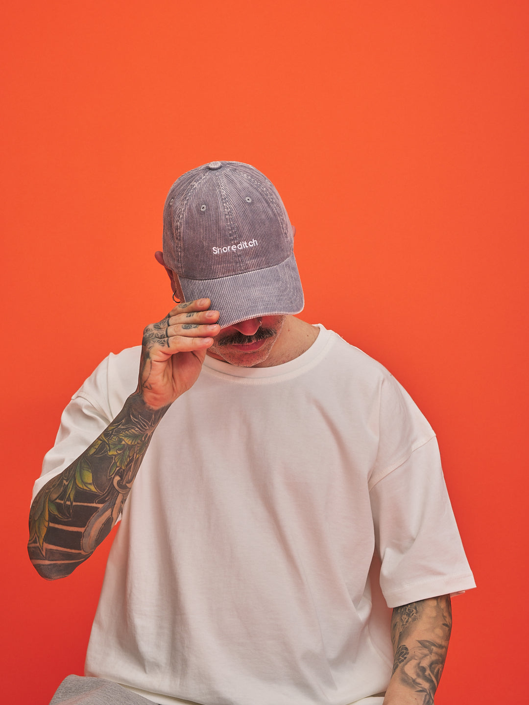 Person wearing a cap with 'Shoreditch' logo against an orange background