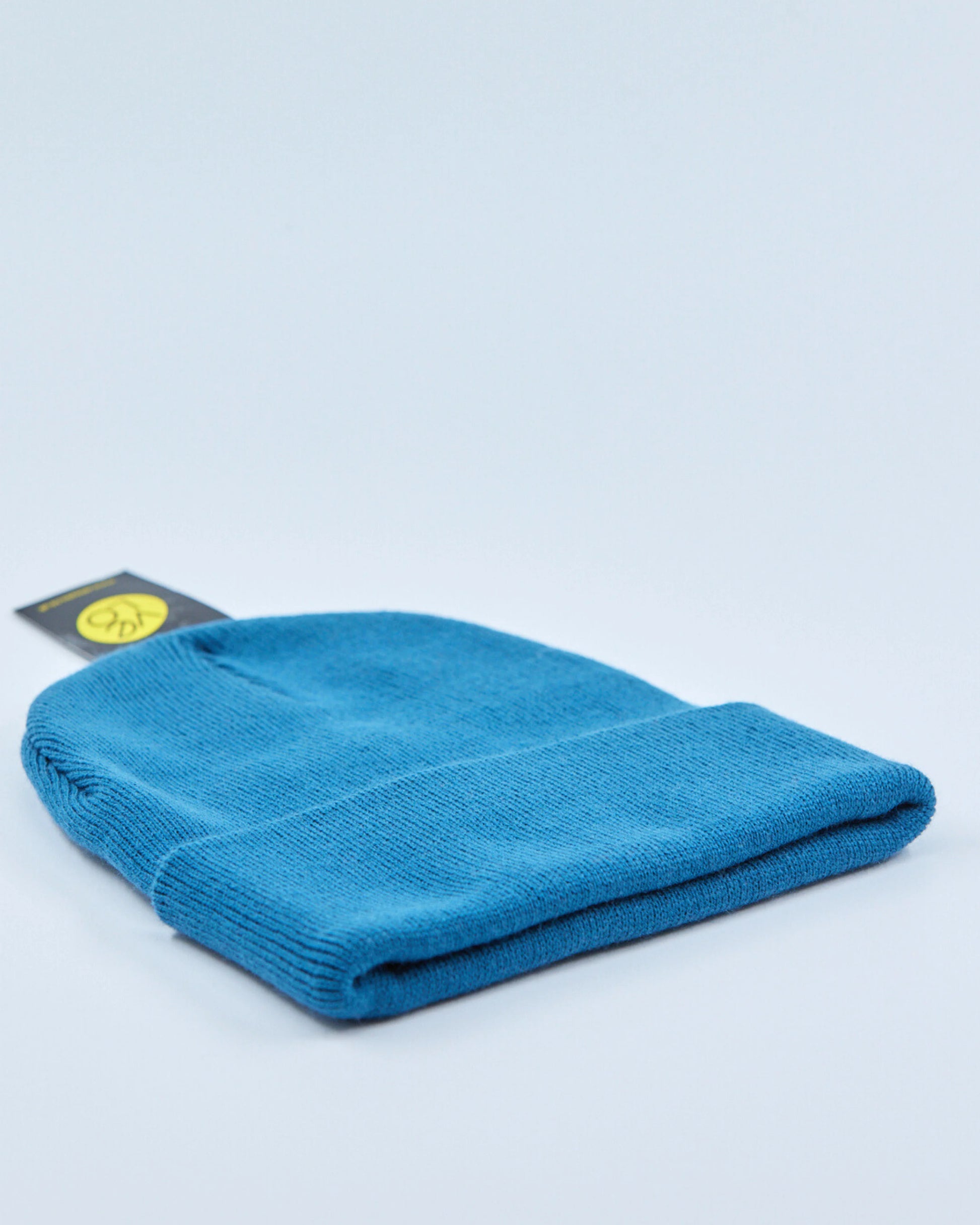 Teal blue beanie with a tag on a light gray background