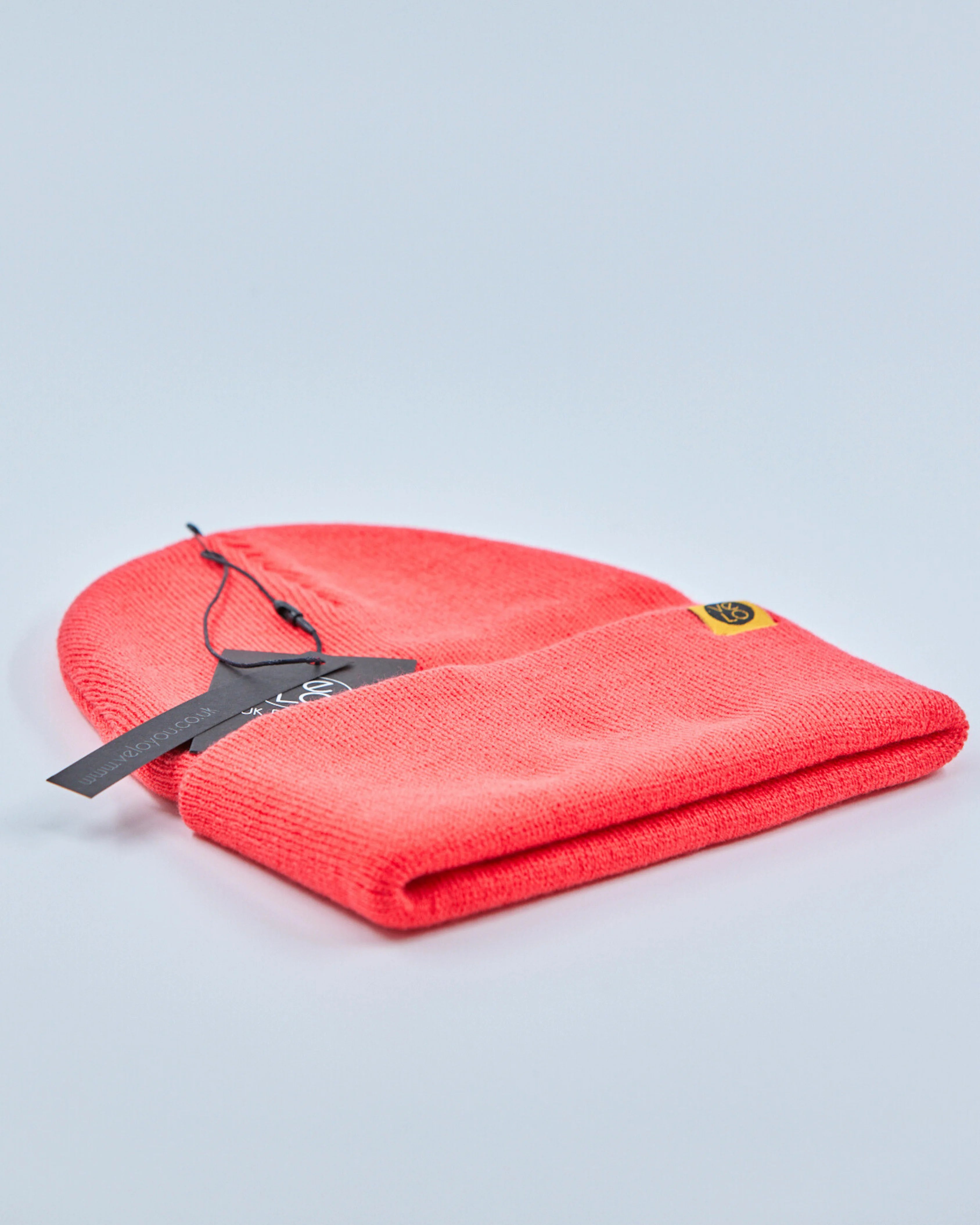 Tomato red beanie with a tag on a light gray background