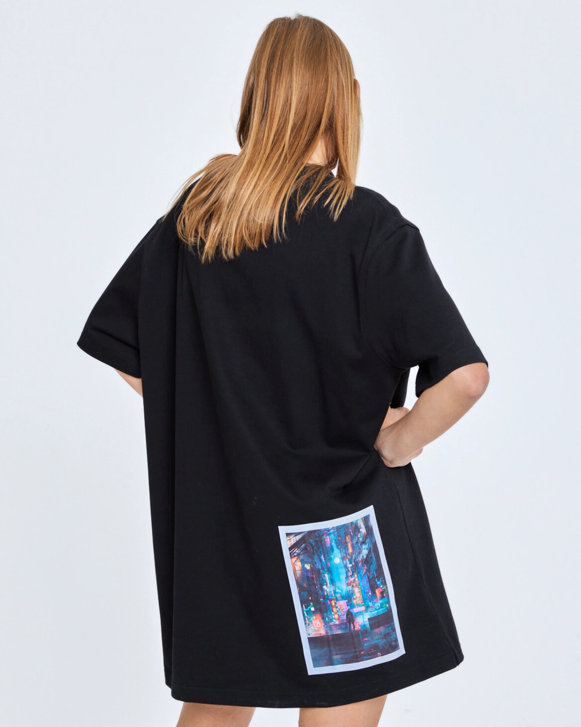 Person wearing a black oversized t-shirt with a colorful graphic on the back against a white background