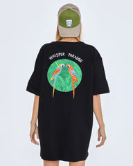 Black t-shirt with parrot design and 'Whisper Paradise' text on the back, worn by a person.