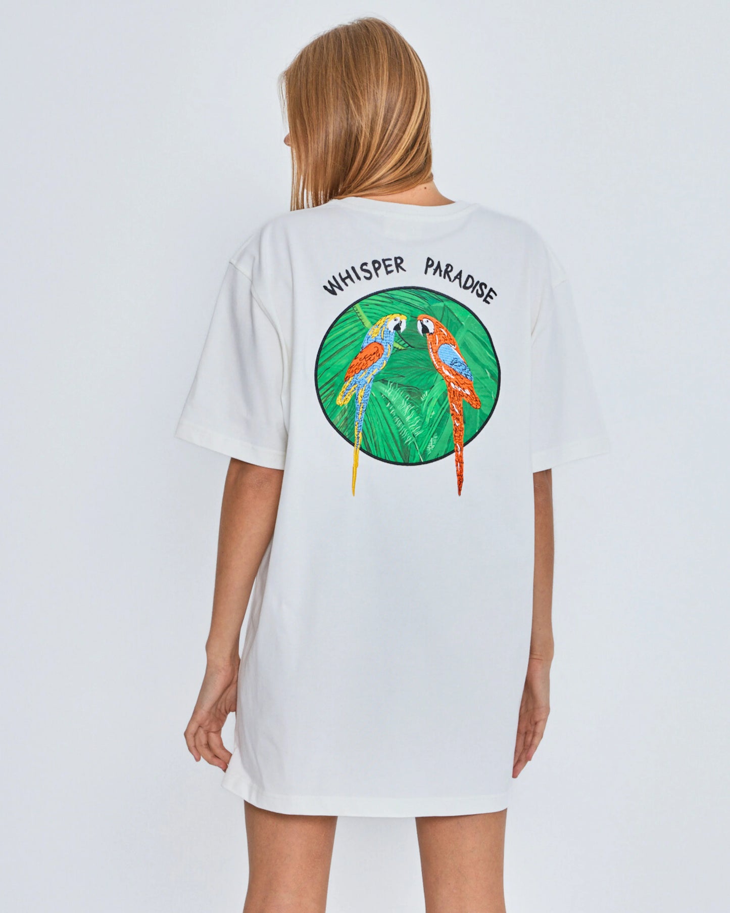 White t-shirt with 'Whisper Paradise' design on the back, worn by a person against a light gray background