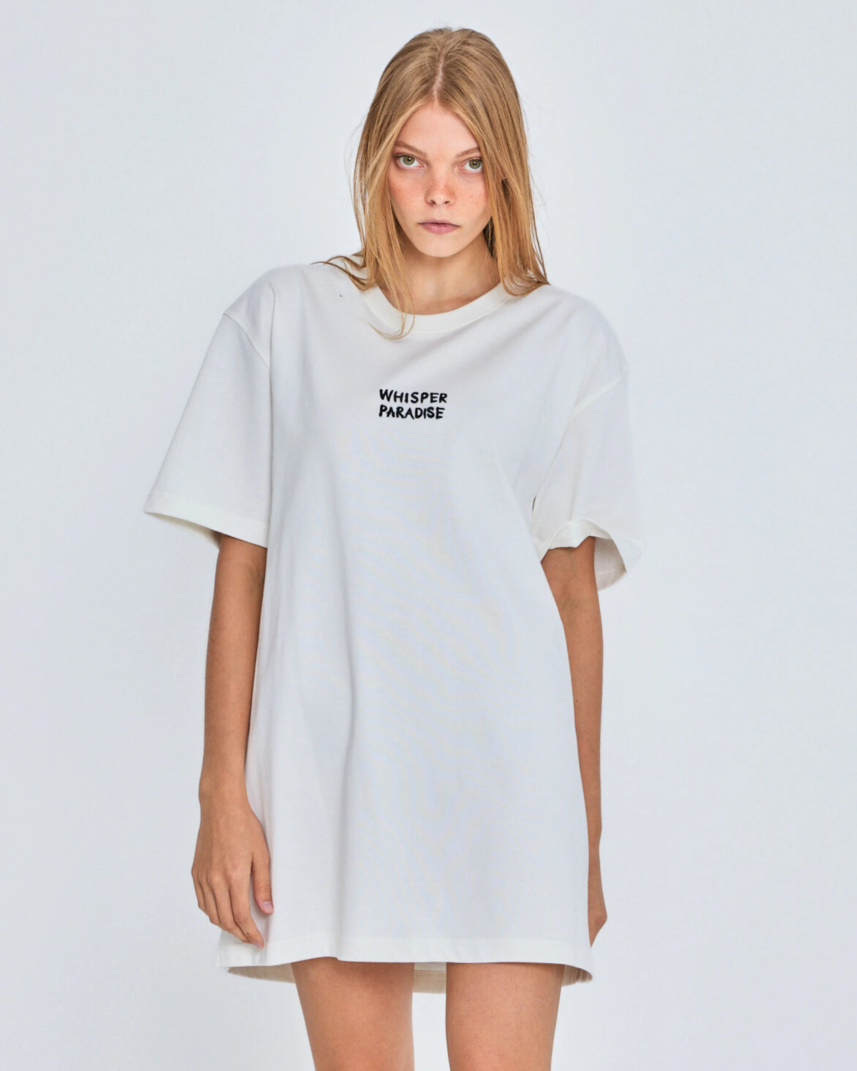 Woman wearing a white oversized t-shirt with text on a plain background