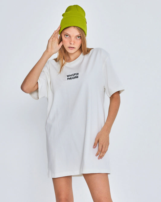 Person wearing a white oversized t-shirt with text and a green beanie on a plain background