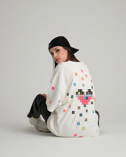Person wearing a white sweater with colourful pixel heart design on a plain background