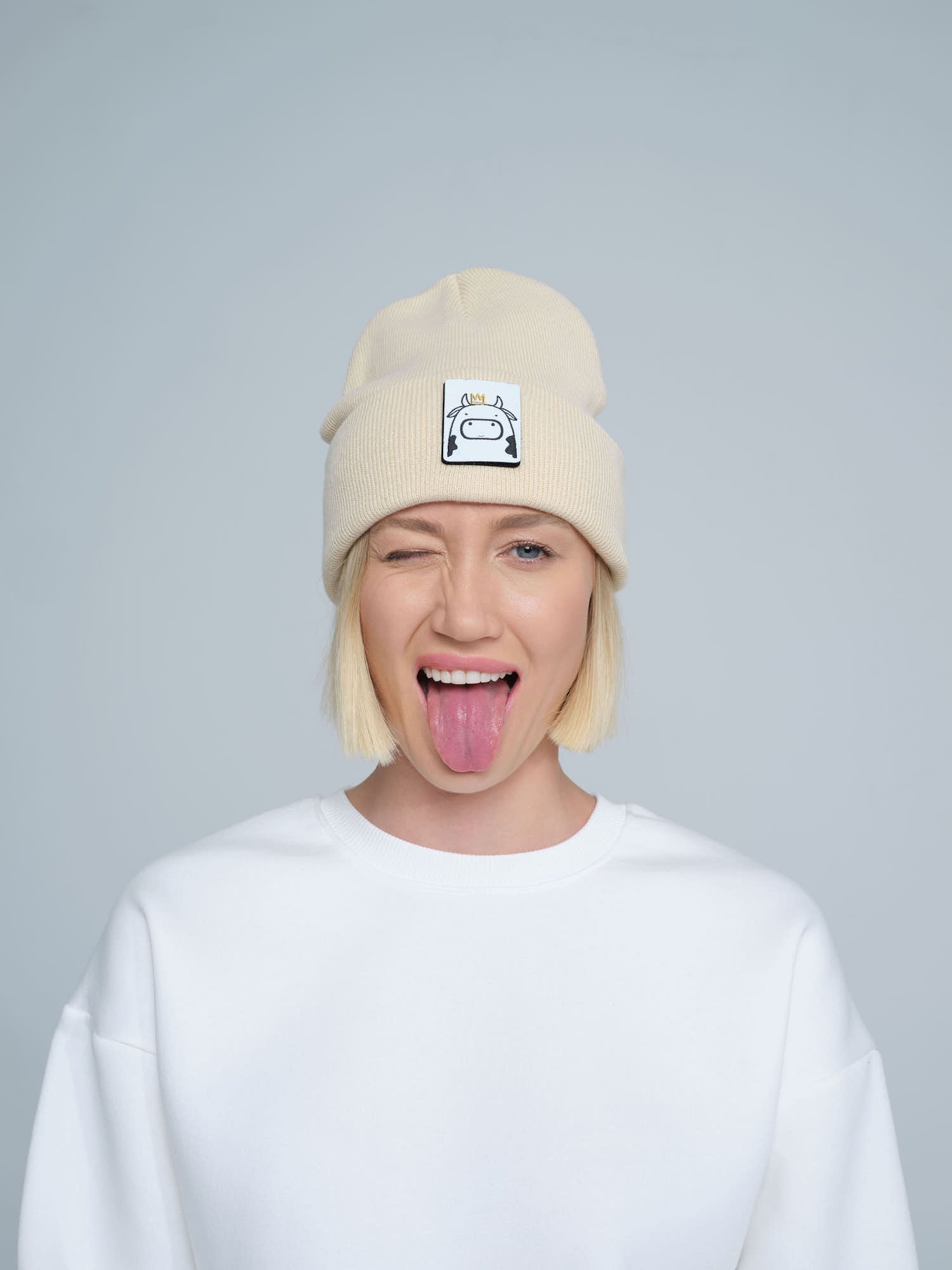 A person wearing a beige beanie hat with a 'cow' design on the cuff, paired with a white t-shirt.