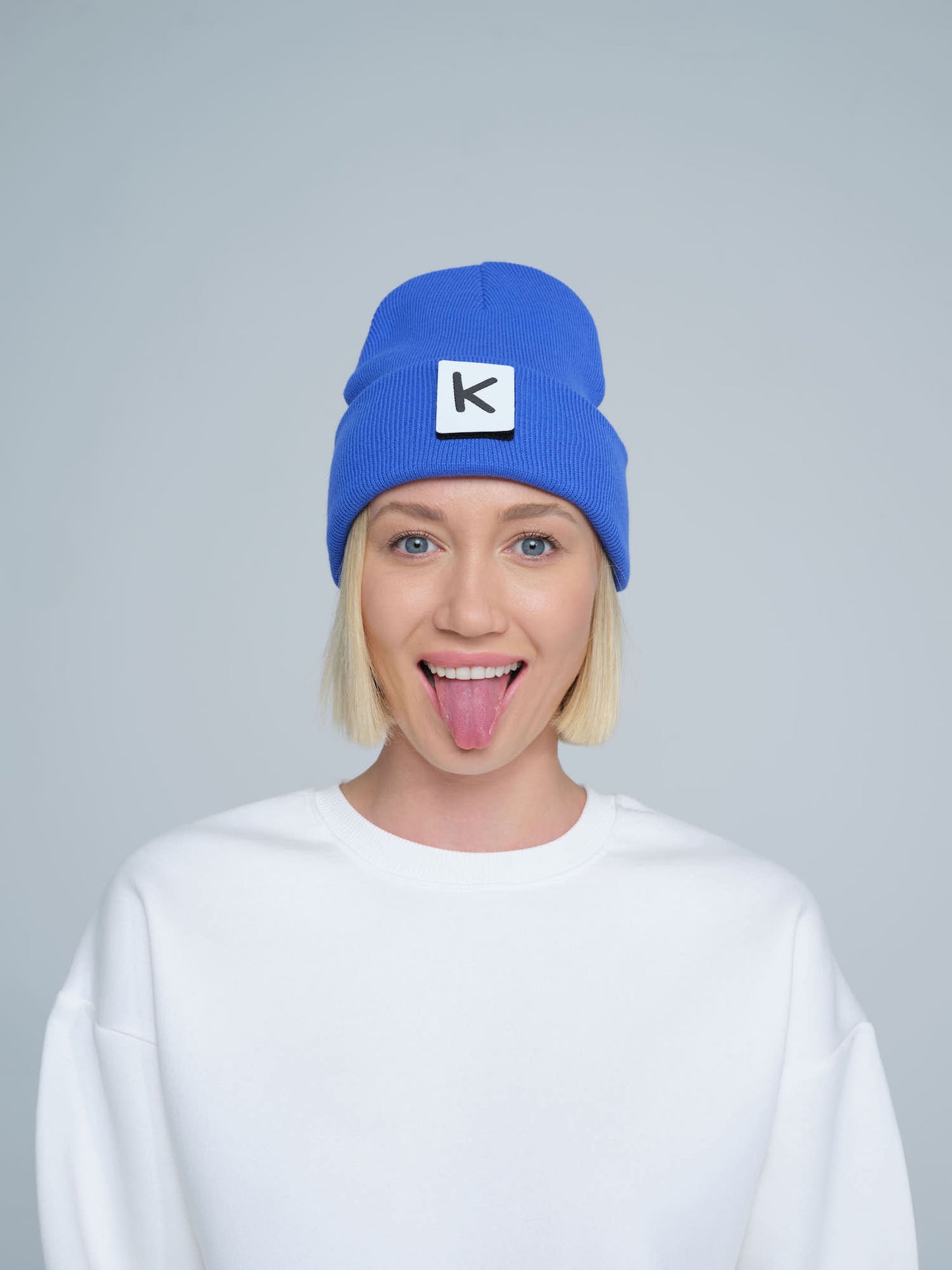 female model wearing blue beanie with K letter patch on it and making a funny face