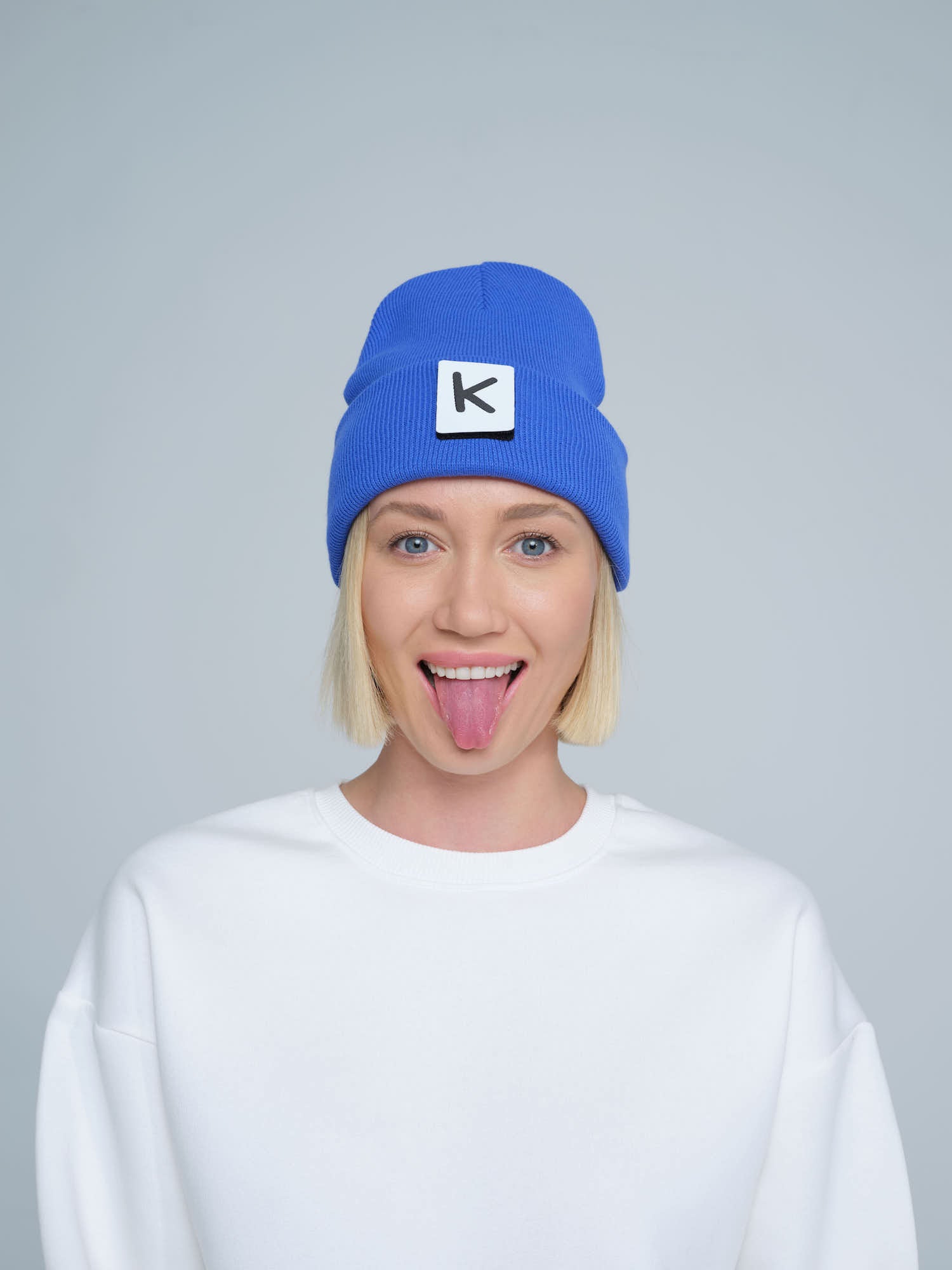 female model wearing blue beanie with K letter patch on it and making a funny face