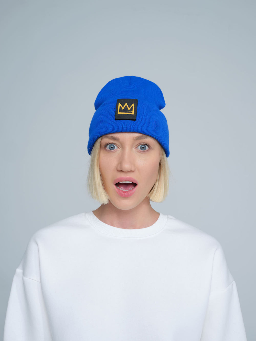 A female person wearing a cobalt blue beanie with a crown design patch on the front.