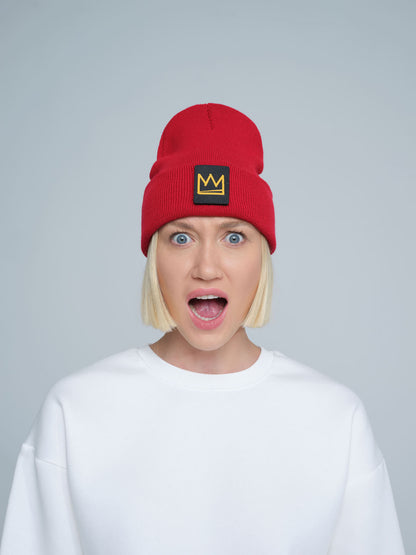 A person wearing a red beanie with a 'crown' design on the cuff, and a white t-shirt.