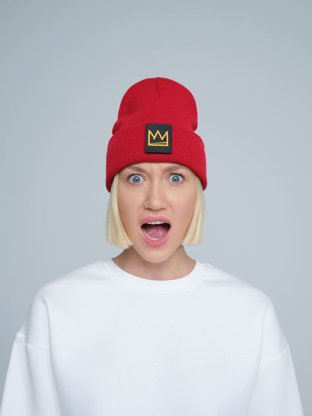 A person wearing a red beanie with a 'crown' design on the cuff, and a white t-shirt.