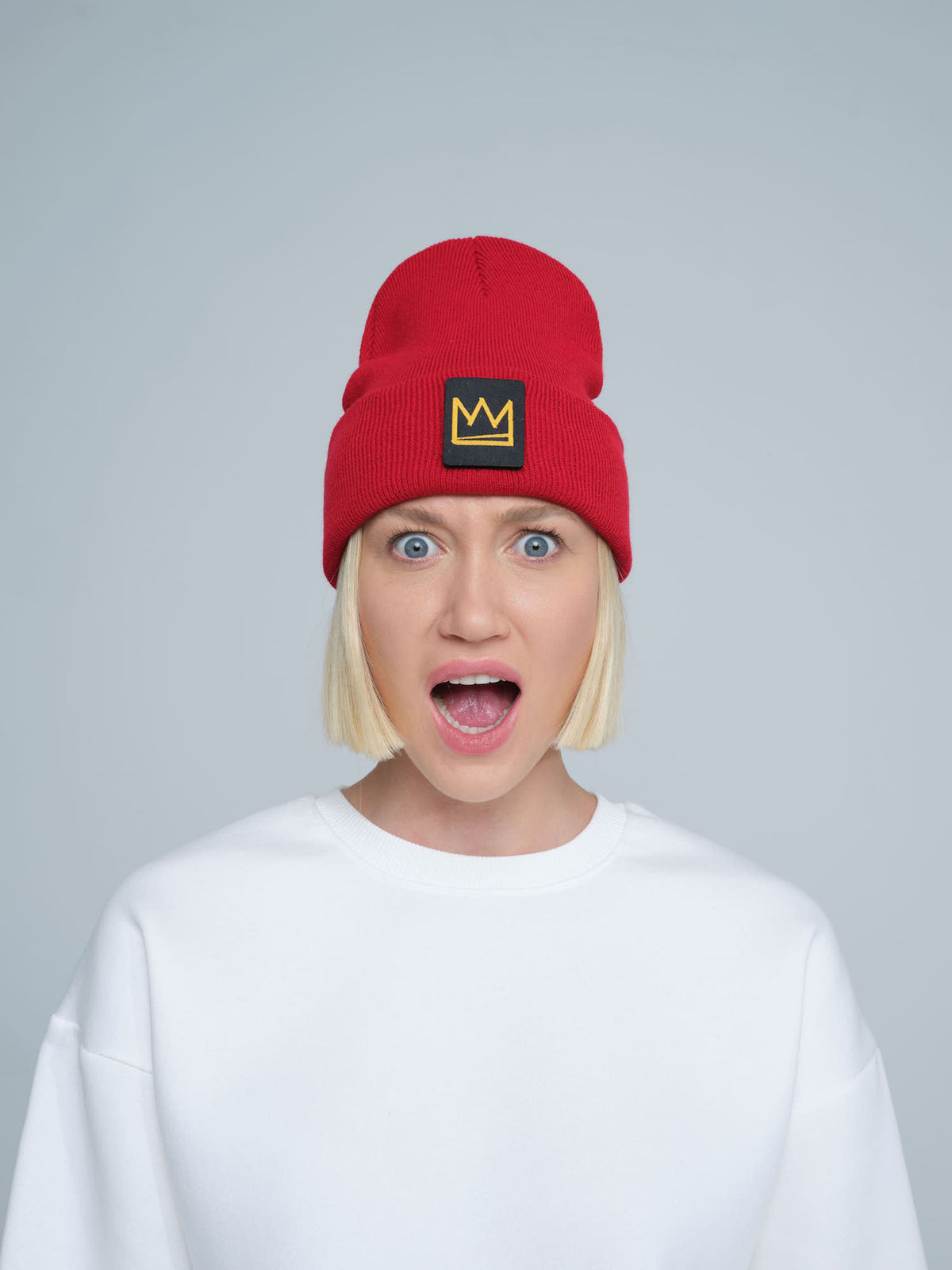 A person wearing a red beanie with a 'crown' design on the cuff, and a white t-shirt.