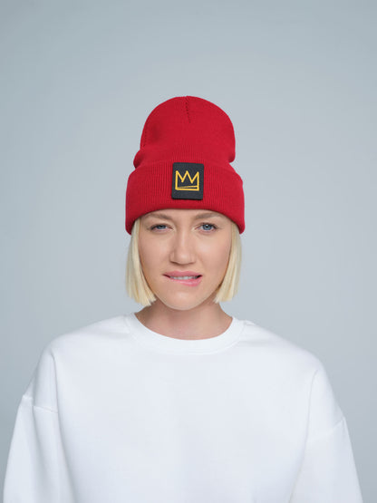 A person wearing a red beanie with a 'crown' design on the cuff, and a white t-shirt.